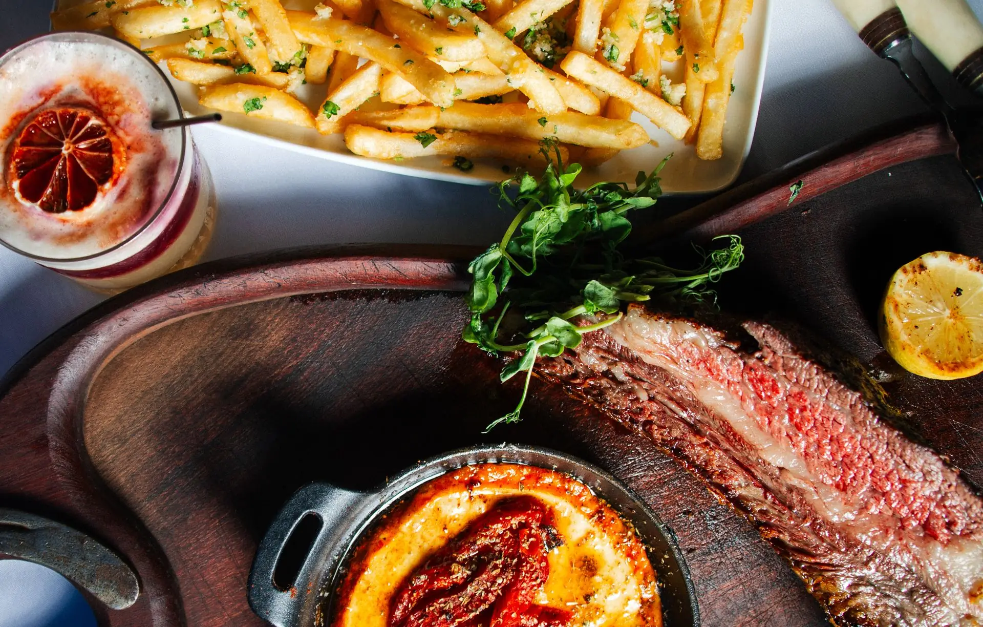 Grilled steak, provoleta in a cast-iron dish and fries on a wooden board